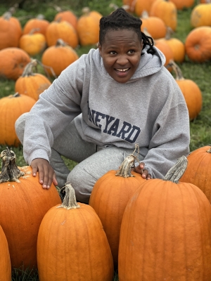 A person in a grey sweatshirt is sitting in front of some pumpkins and smiling