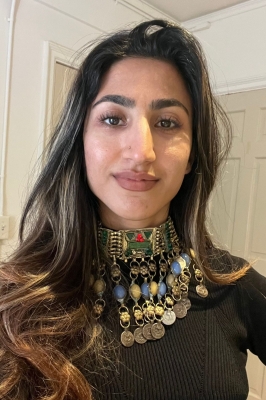 A young woman with long brown hair with blond ends wears a beautiful, elaborate silver and beaded nacklace with a black shirt. She is smiling into the camera.