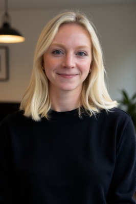 A young woman with shoulder-length blond hair and a black sweater smiles into the camera.