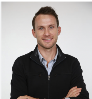 Andrew Savage smiling in front of a white wall 