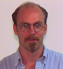Jeffrey Carpenter, short brown hair, round glasses, mustache and beard with blue collared shirt
