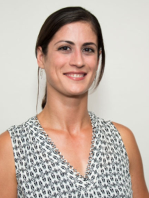 Margaret Hanson, dark hair pulled back into ponytail with V-neck, sleeveless, multi print shirt.