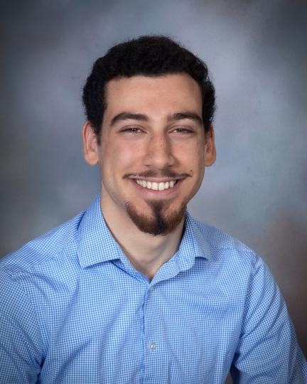 Omar wearing a blue shirt, unbuttoned at the collar, against a grey background