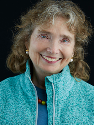 2021 headshot of Maggie Paine, wearing a light aqua sweater over a blue shirt with multicolored bead necklace