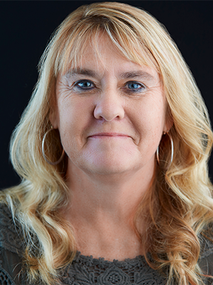 headshot of Brenda Currier wearing dark green woven top and silver hoop earrings