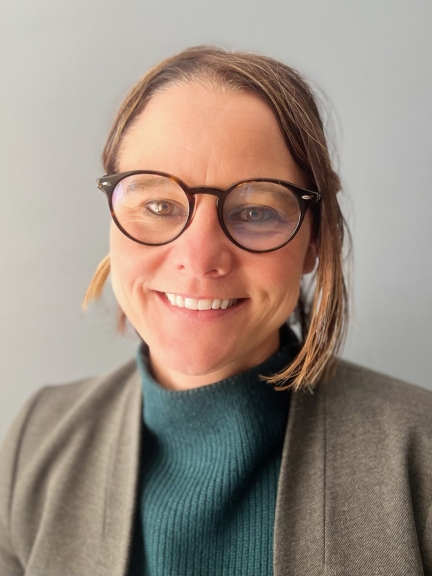 Photo of Heather Pena - a woman with short hair, wearing glasses, a teal sweater and blazer, smiling