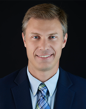 Eamon Del Giacco in dark jacket over light blue buttoned shirt with green-and-blue plaid tie