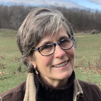 Ellen stands in a field wearing a black turtlenect