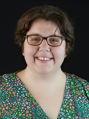 Tessa Hunter in glasses and in a multicolored green, blue, orange and purple speckled top