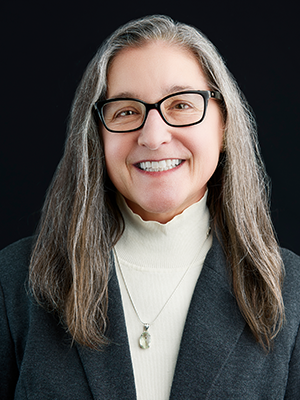 Deb Wales in beige sweater and dark gray cardigan wearing glasses.