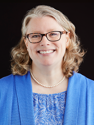 Laurie Celik wearing a blue floral blouse with blue cardigan and gold necklace