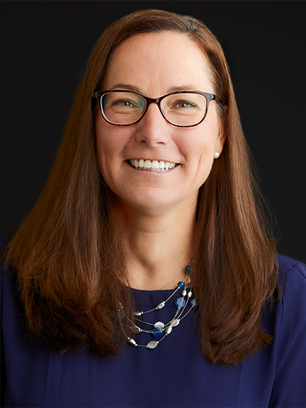 Portrait of Jessica Buxton wearing a dark blue blouse, glasses, and a white necklace.