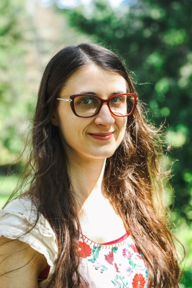 image of headshot of Tabitha smiling and wearing glasses in a summer background