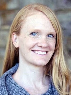 Female with long auburn hair and grey, heathered, cowl-necked  shirt