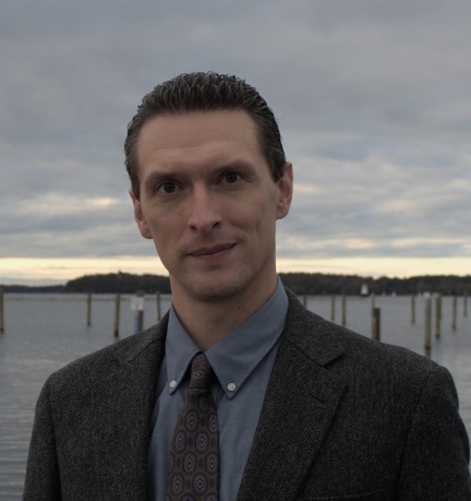 Male with slicked back dark hair wearing a suit and tie.