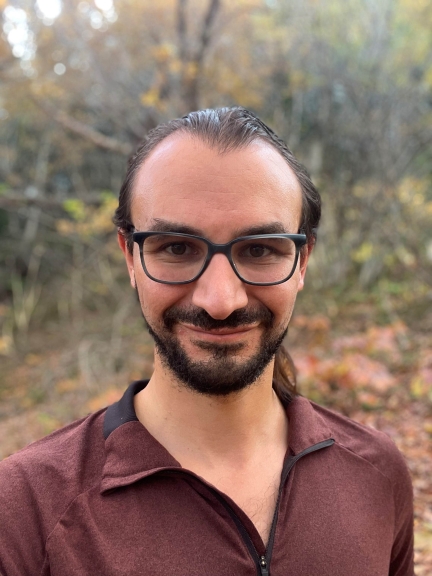 Man with mustache, beard, and dark rimmed glasses wearing deep burgundy/brown half-zip shirt with collar