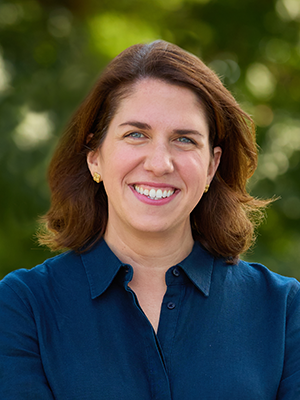 Molly Birenbaum in deep blue collared blouse with leafy trees in background
