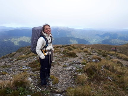 A smiling person on a mountain top with a backpack.