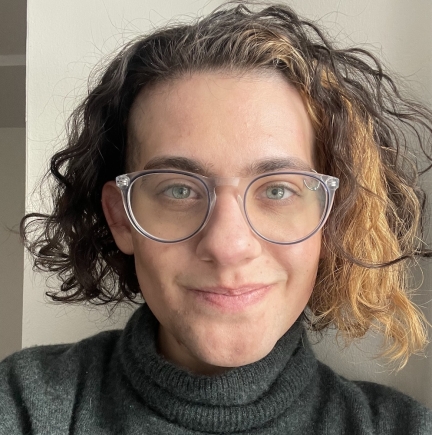 White skinned human with curly dark and light hair cut above the shoulders. Person wears glasses