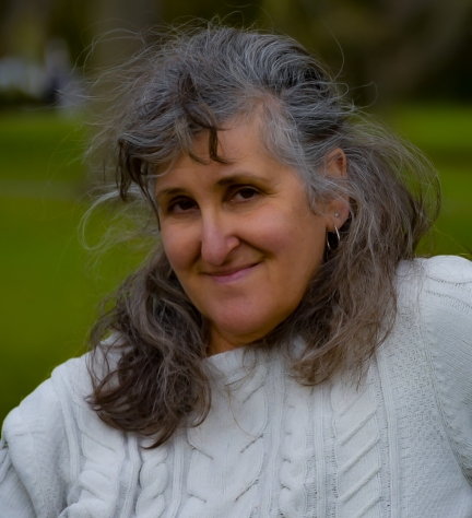 A Woman with salt and pepper shoulder length hair wearing a white sweater