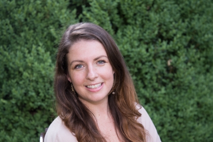 A smiling woman with dark hair in front of a green outdoor backkground
