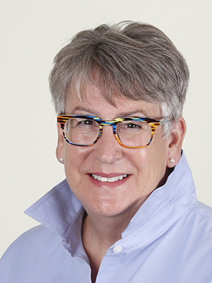 Beth White in colorful glasses and a button-up with the collar popped