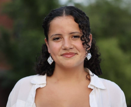Young woman with dark curly hair and a white blouse smiling at camera