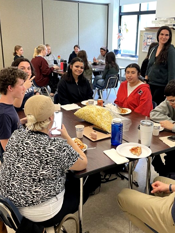 Groups of people gather around tables, eating.