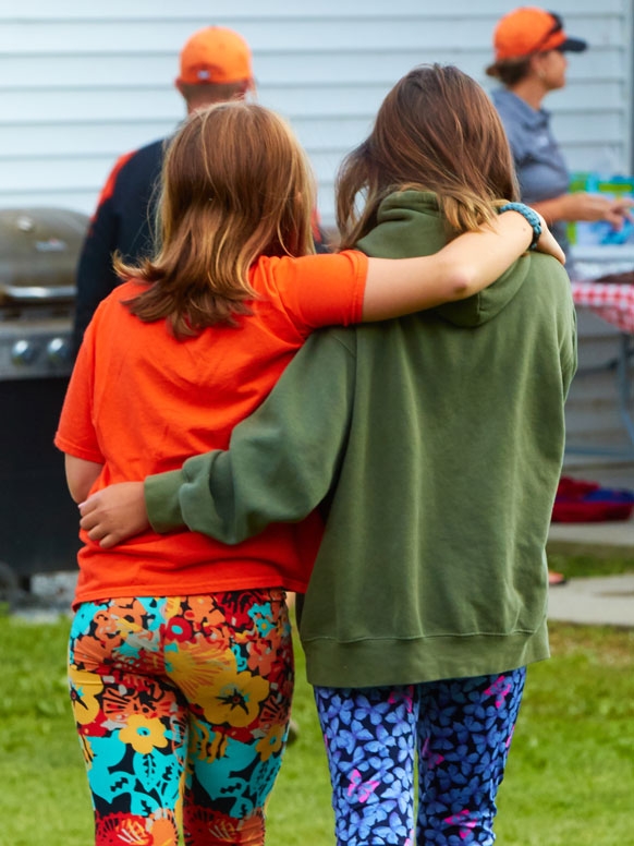 Two elementary school children photographed from behind with their arms around each other.