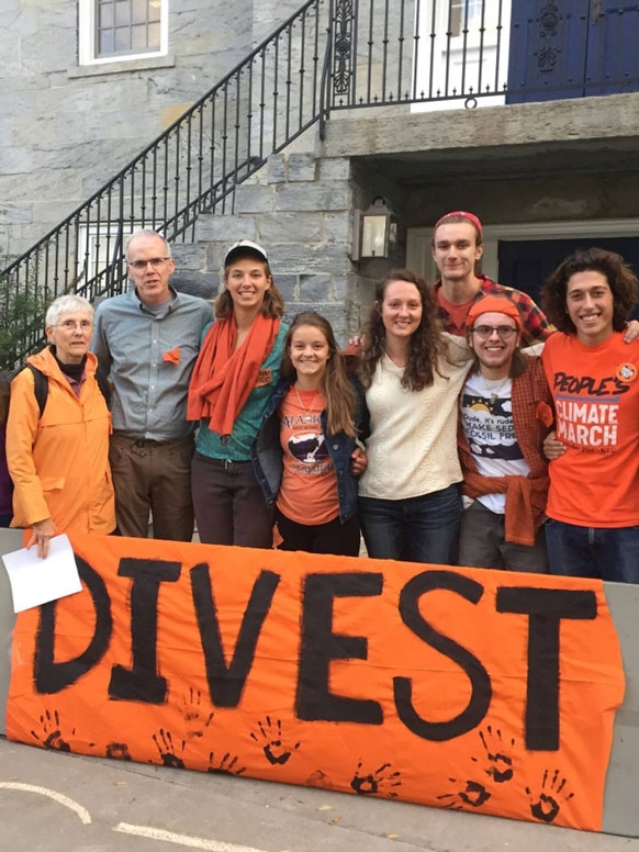 A group os people of all ages stand by a large sign that reads "Divest."