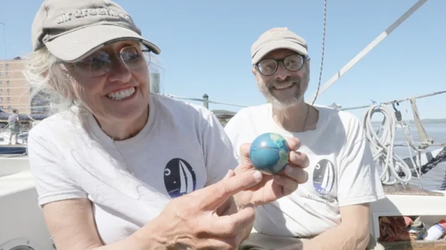 Robin Bell ’80 and Karl Coplan ’80 on their boat holding a small glog while smiling.