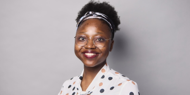 Michell Mamombe wears a polka dot shirt and smiles in front of a grey photo backdrop.