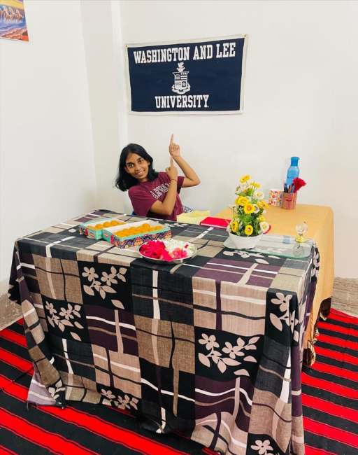 A person sits smiling at a table with materials and points at a Washington and Lee University banner.