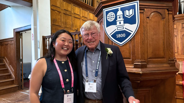 Emily Ballou ’21 and Will Jackson ’51 stand smiling together in front of the podium of the Middlebury Chapel