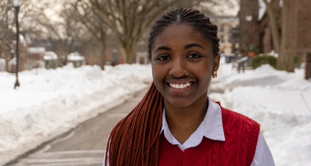 A person looks at the camera with a smile. It's winter, there is snow behind them, but it doesn't seem cold.