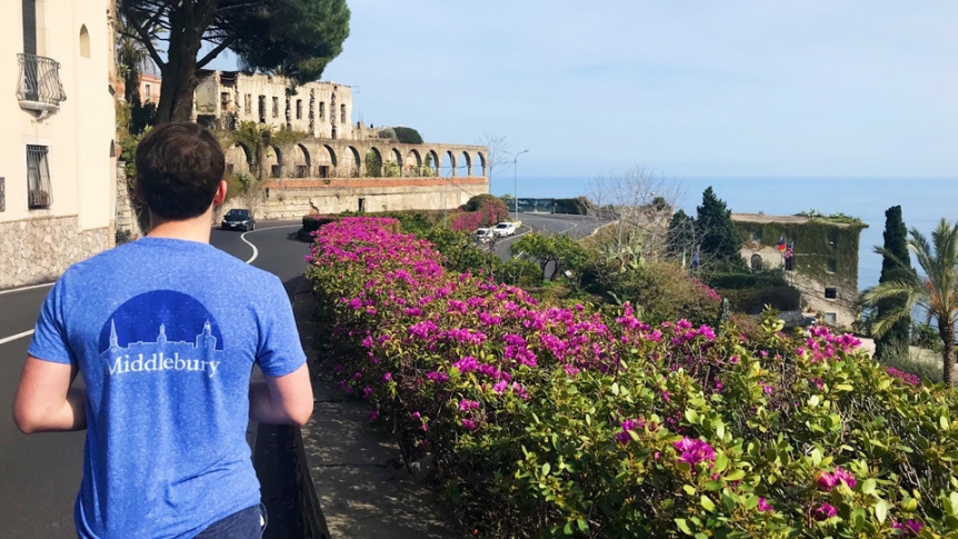 Back of male student walking along road next to ocean.