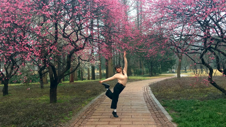 Female student posing on sidewalk among crab apple trees.