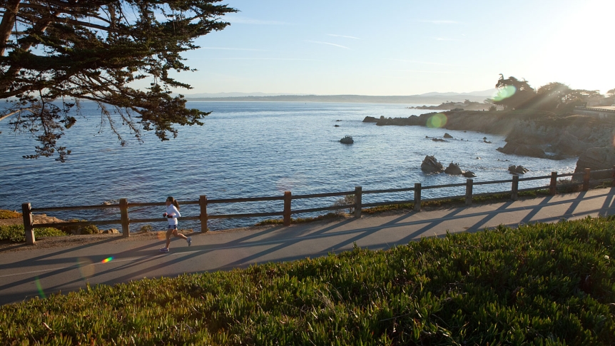 A young woman jogs along the Monterey Coastal Trail at dusk.