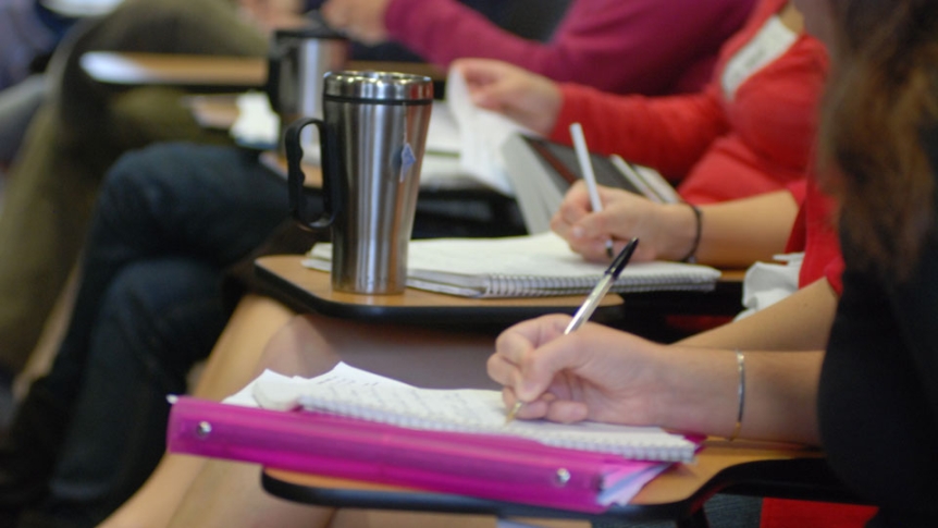 Close up of students writing in notebooks.