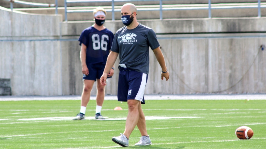 A Middlebury football player and coach participate in practice wearing masks.