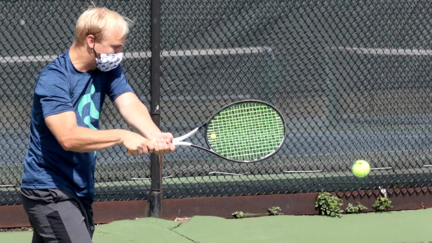 A Middlebury tennis player practices on the court wearing a mask.