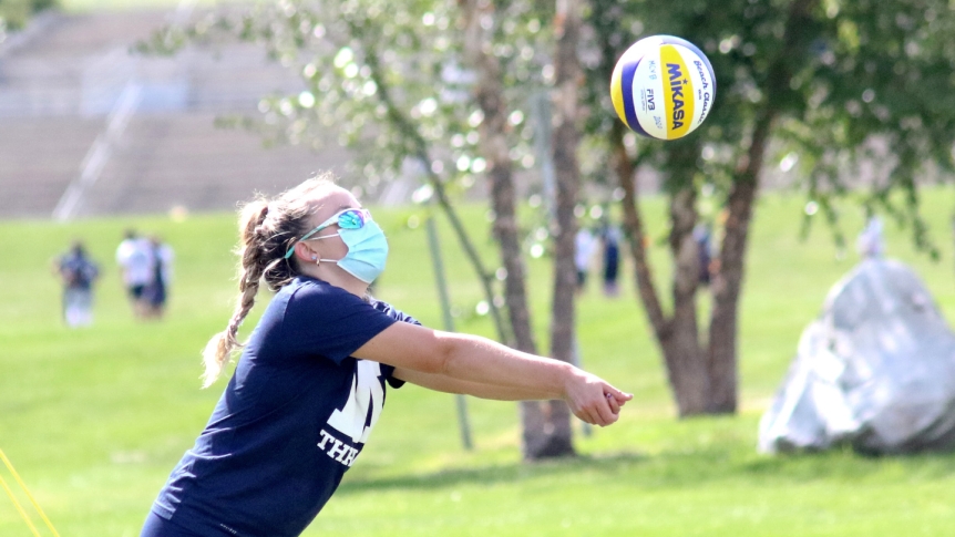 A female Middlebury student practices volleyball wearing a mask.