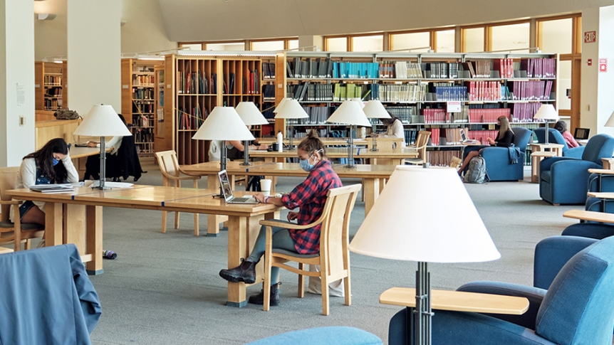 Students sit wearing masks and studying in library.