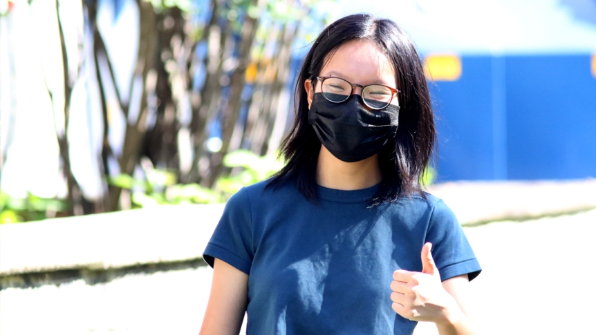 A female Middlebury student walks wearing a mask giving the thumbs up