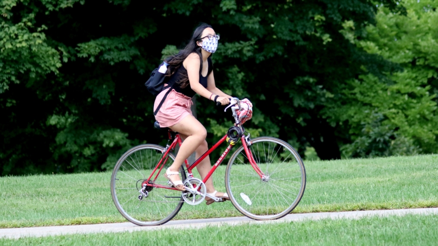 A female Middlebury student rides her bike on campus wearing a mask