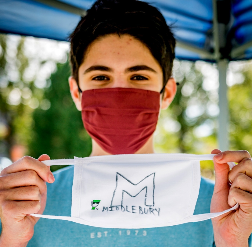 A Middlebury student holds up a mask with a hand-drawn "Middlebury" logo