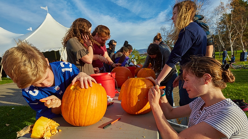 College student and community children carve pumpkins 
