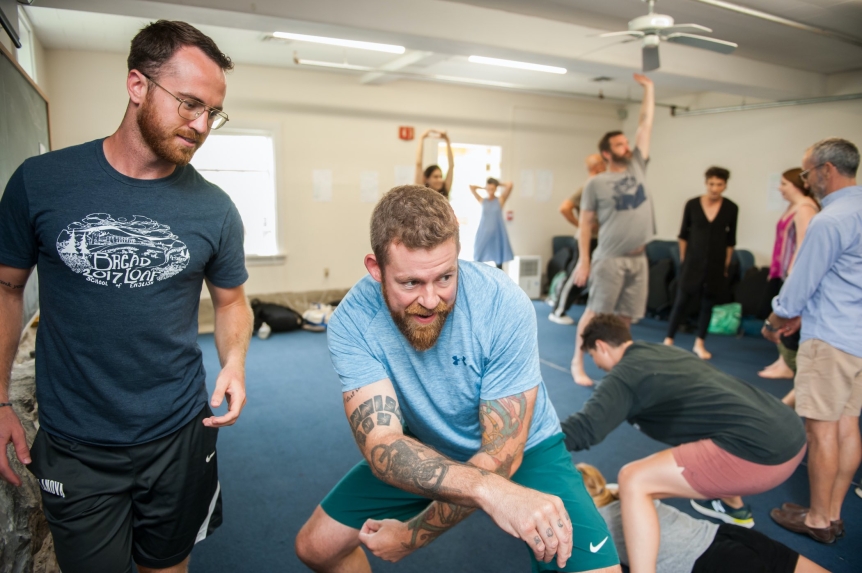 man in a classroom full of people leans forward in a stance while in acting class