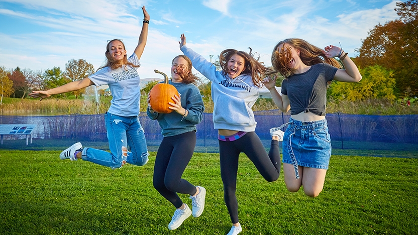Four  Middlebury students jump in the air during Harvest Fest