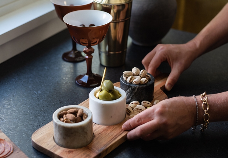 Hands reaching into frame place a tray of olives and nuts 